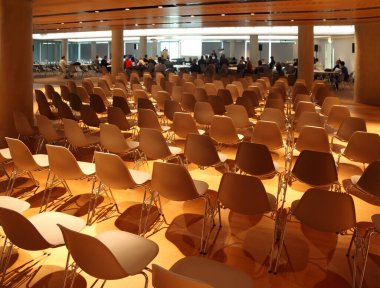 Birkaç sıra beyaz plastik sandalye; açık konferans odasındaki insanlar