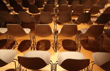 Sarı zeminde metal bacaklı birkaç sıra beyaz plastik sandalye.