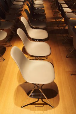 Sarı zemin üzerinde krom kaplama bacaklı beyaz plastik sandalyeler.