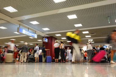 Havaalanı koridorunda bekleyen insanlar var. İnsanlar bavullarıyla hareket eder.
