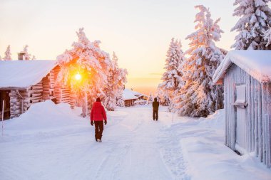 Back view of kids walking among wooden huts and snow covered trees in Lapland Finland clipart
