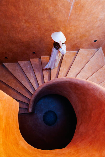 Beautiful woman wearing white dress and conical hat walking down spiral staircase