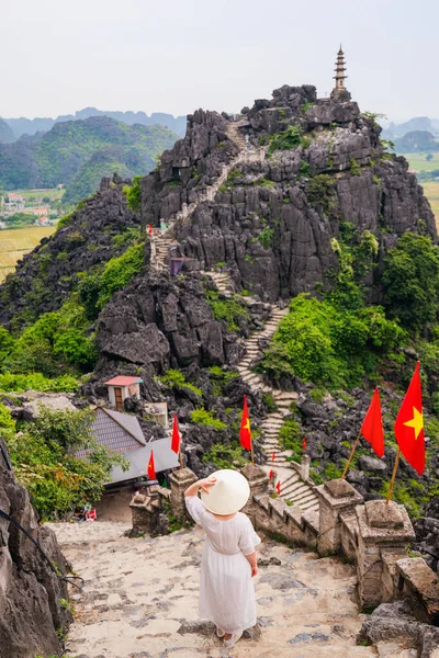 穿着白色衣服头戴锥形帽子的漂亮女人的背影欣赏着越南摩阿洞喀斯特山脉的壮丽景色 免版税图库图片