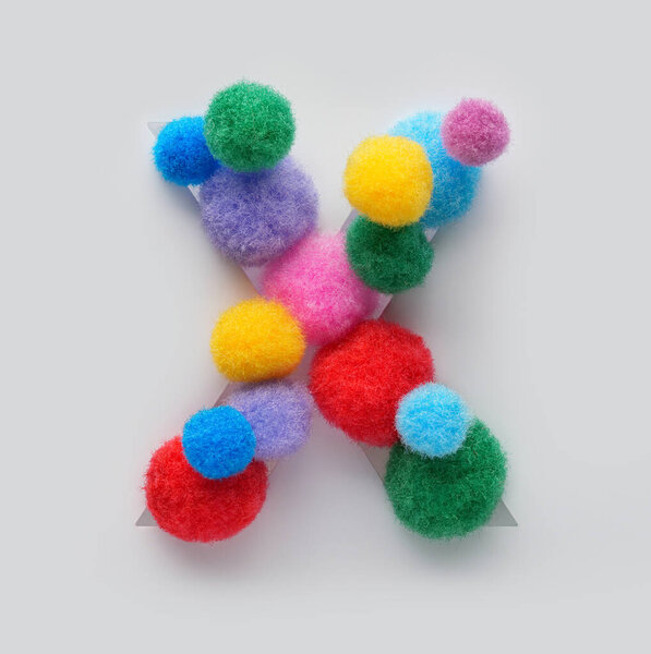 Цветная буква X из пушистых помпонов на белом фоне. Творческая ручная типография для детей, изучающих алфавит, образовательный дизайн, игровой декор класса и графические проекты.