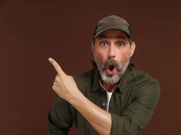 Middle-aged Caucasian country man expresses extreme surprise, pointing his finger to the side. Copy space. Advertising concept. High quality photo