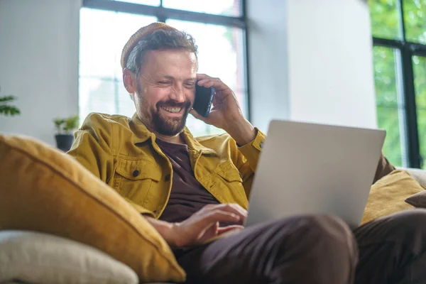 Homem Sorridente Conversando Telefone Enquanto Trabalhava Laptop Sofá Escritório Ele — Fotografia de Stock