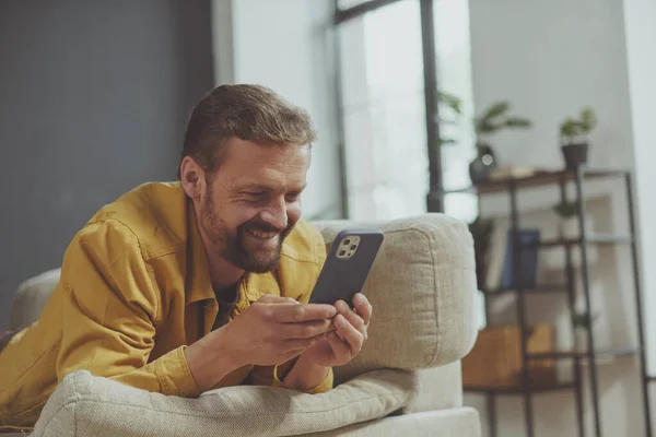 Glad Smilende Mand Sms Telefonen Mens Liggende Sofaen Derhjemme Mand - Stock-foto