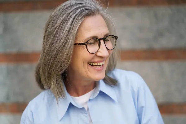 青いシャツを着ているメガネを持つ幸せな年上の女性 ロイヤリティフリーのストック写真