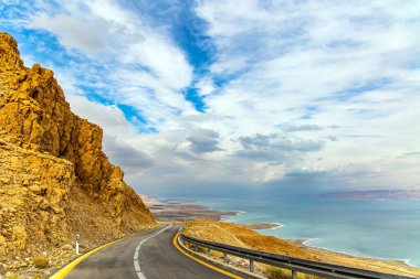 İsrail kıyıları. Otoyol Ölü Deniz kıyısı boyunca uzanıyor. Deniz yüzeyi bulutları yansıtır. Doğanın en büyük harikası Ölü Deniz 'dir. Bulutlu ve açık Ocak günü. 