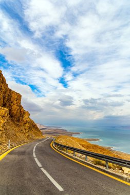 Otoyol Ölü Deniz kıyısı boyunca uzanıyor. Bulutlu ve sıcak Ocak günü. Deniz yüzeyi bulutları yansıtır. İsrail kıyıları. Doğanın mucizesi - Ölü Deniz.