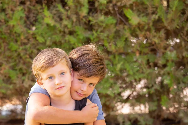 全家福两个可爱的男孩拥抱在一起 哥哥的头发是棕色的 眼睛是绿色的 弟弟的头发是金色的 眼睛是蓝色的 兄弟们温暖的春日 — 图库照片