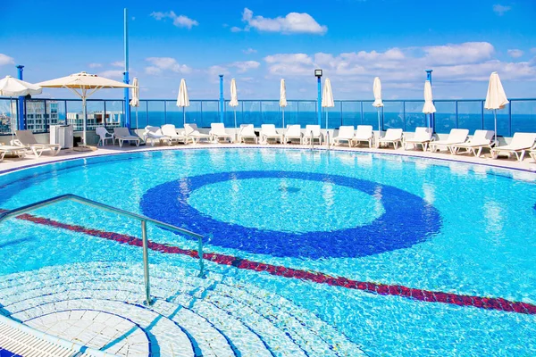 Rooftop pool of a high-rise hotel. The round bowl of the pool is filled with clean, transparent water. Around the pool, sun loungers are waiting for guests. Tel Aviv, Israel