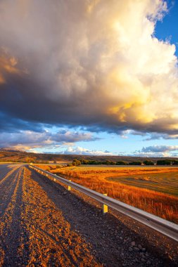 Gigantic scenic thundercloud illuminated by the sunset. The steppe is overgrown with orange grasses. The endless Argentinean prairie and the famous dirt road Ruta 40. 