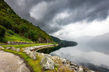 Batı Norveç 'in dağlarındaki manzara yolu. Hardangerfjord 'un başlangıcı. İskandinavya. Yaz. Güçlü bulutlar fiyordun su yüzeyine yansıyor..  