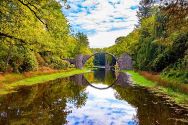 Rakots Nehri 'ndeki Şeytan Köprüsü. Park Kromlau, Almanya. Köprünün bazalt sütunları sudaki yansımalarıyla mükemmel bir daire oluşturur. Parkta resim gibi dar bir köprü