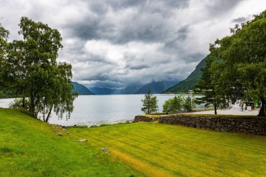 Güçlü bulutlar fiyordun su yüzeyine yansıyor. Su ve yeşillik krallığı. Hardangerfjord 'un başlangıcı. Batı Norveç 'in dağları. Yaz, Temmuz. 