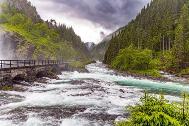 Güçlü çifte şelale Lotefossen. Yaz yağmurlu bir gün. Yol su püskürtülerinden geçiyor. Havada bir su tozu bulutu asılı duruyor. Norveç 'e git. Odda Komünü