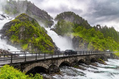 Güçlü çifte şelale Lotefossen. Temmuz yağmurlu bir gün. Şelale erime ve yağmur suyuyla beslenir. Yol su püskürtülerinden geçiyor. Havada sarkan su tozu bulutu. Norveç 'e Seyahat. 