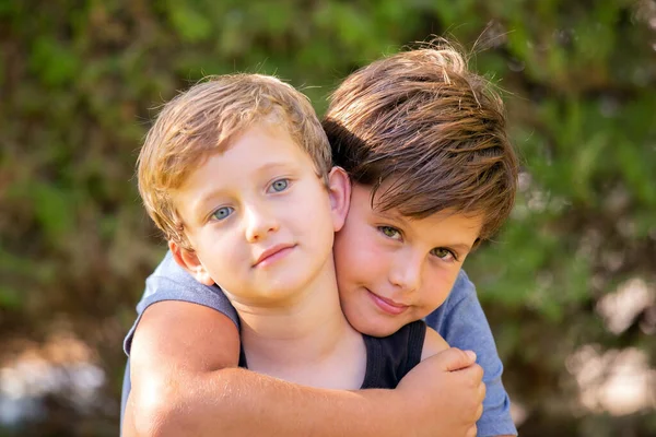 两个可爱的男孩拥抱在一起 哥哥的头发是棕色的 眼睛是绿色的 弟弟的头发是金色的 眼睛是蓝色的 兄弟们全家福温暖的春日 — 图库照片