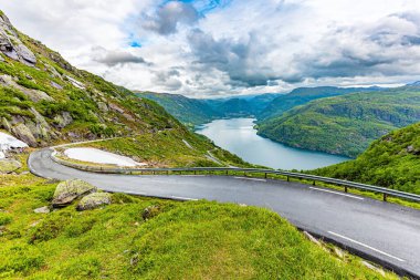 Dar dağ yolu. Gölü çevreleyen yeşil kayalar. Norveç 'te soğuk Temmuz. Dağların yamaçlarında kar tarlaları kaldı. 520 nolu yolda karavanla seyahat ediyoruz.. 