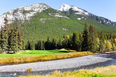 Kıçı çakıllı sığ bir akıntı. Rundle ve Cascade Dağları 'nın eteklerindeki golf sahaları. Kanada 'nın Rocky Dağları. Sonbahar Hindistan yazında güneşli bir gün.. 