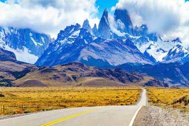 Fitzroy Dağı 'na giden yol. Arjantin Patagonya 'sı. Meşhur en tepedeki kaya tekelleri güneş tarafından aydınlatılır. Sonsuz düzlükler sarı sonbahar otlarıyla kaplıdır.