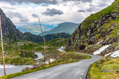 Yağmurdan parlayan tehlikeli dağ yolları. Yol kenarı yüksek direklerle işaretlenmiş. 520 nolu yolda karavanla seyahat ediyorum. Gri kayalar gölün etrafını sarar. Norveç 'te soğuk yaz.