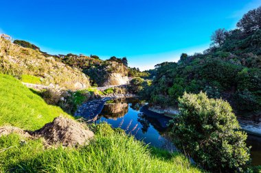 The picturesque Vaipingau Stream reflects hills, bushes and high reeds in the water. The magnificent nature of New Zealand. Sheer White Cliffs of the Pacific coast of northern Taranaki. 
