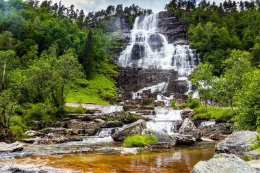The colossal roaring waterfall Twindefossen. Summer day in the mountains of Norway. Exciting adventure in the north of Norway. Travel north. Picturesque green country in summer.