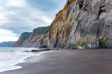 Kuzey Taranaki 'nin Pasifik kıyısındaki Saf Beyaz Kayalıklar. Yumuşak kum üzerindeki ince su tabakası gökyüzünü yansıtır. Pasifik Okyanusu 'nda gelgit var. Yeni Zelanda 'nın görkemli doğası. 