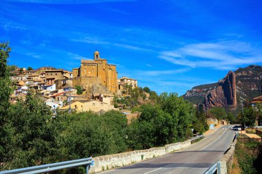  Asphalt highway passes through the rocks. The Mallets of Riglos. Hoya de Huesca, Aragon. Part of the foothills of the Pyrenees. Hot sunny afternoon. Romantic trip to Spain. 