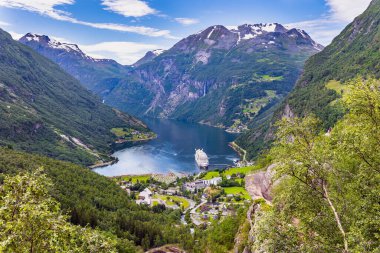 The largest, most beautiful and famous Norwegian fjord Geiranger. Snow-white ocean liner is moored at the pier. Warm sunny day in July. Summer trip to Norway.