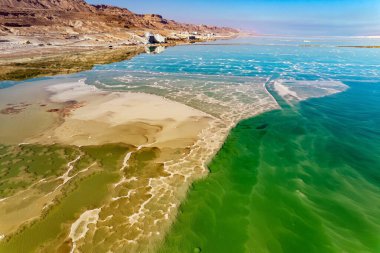 The clear green water of the salty sea is surrounded by pink mountains. Salt deposits are visible on the seabed. Magic of the Dead Sea. The photo was taken from a drone. Cold sunny day. Israel