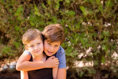 Two wonderful boys are hugging. The older brother has brown hair and green eyes, the younger brother is blond with blue eyes. Warm spring day in a green park. 
