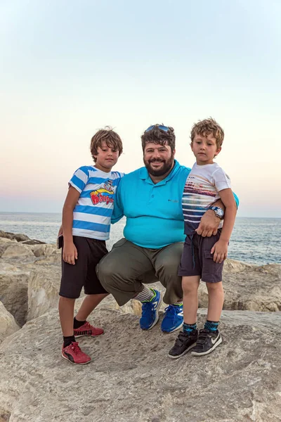 Happy father with two sons. Family vacation in a hotel on the Greek island of Cyprus. Rocky shore of the Mediterranean Sea.