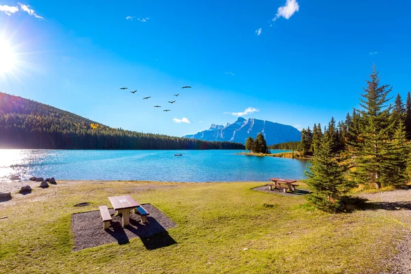 Two Jack Lake. Cozy picnic table and benches. Huge glacial lake reflects the sun. Travel to Canada, the Rocky Mountains. Beautiful autumn day.