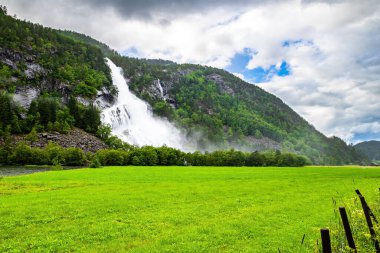 Norveç. Çok güçlü bir şelale Vidfossen. Batı Norveç 'in dağlarındaki manzara yolu. Beyaz su köpüğü şelalenin ayağını kaplar. İskandinavya. Yaz, Temmuz.