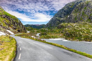 Yağmurdan parlayan tehlikeli dağ yolları. Yol kenarı yüksek direklerle işaretlenmiş. 520 nolu yolda karavanla seyahat ediyorum. Gri kayalar gölün etrafını sarar. Norveç 'te yaz.