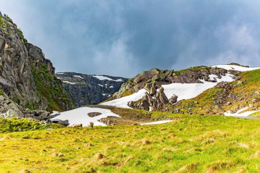 Norveç 'te soğuk bir yaz. Şiddetli gri bulutlar gökyüzünü kaplıyor. 520 nolu yolda karavanla seyahat ediyorum. Geçen yılın karı ve gri gökyüzü. Koyun sürüsü yol kenarında otluyor..