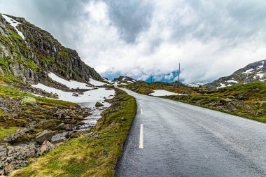 Yağmurdan parlayan tehlikeli dağ yolları. Gri kayalar gölün etrafını sarar. Ağır bulutlar gökyüzünü kaplıyor. Norveç 'te soğuk bir yaz. 520 nolu yolda karavanla seyahat ediyoruz.. 