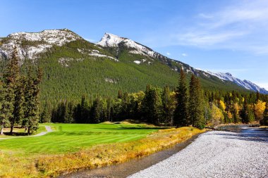 Kanada 'nın Rocky Dağları. Rundle ve Cascade Dağları 'nın eteklerindeki golf sahaları. Kıçı çakıllı sığ bir akıntı. Sonbahar Hindistan yazında güneşli bir gün.