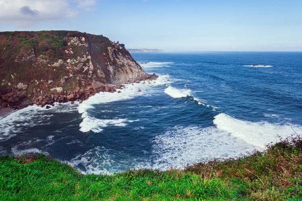 Huge waves of surf beat against stone breakwaters. Magnificent Atlantic Ocean. Asturias. Picturesque fishing port of the city of Luarca in the bay. Romantic trip to Spain.