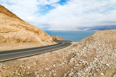 Deniz kıyısındaki muhteşem asfalt yol. Dünyanın en tuzlu denizi, Ölü Deniz. Musevi Çölü dünyadaki en ünlü çöllerden birisidir. İsrail, kış bulutlu bir gün. 