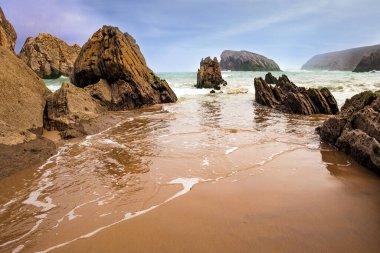 Plajın yumuşak ıslak kumu kayalık kayaları yansıtır. Playa de la Arnia plajı. Kar beyazı deniz köpüğü parlıyor. İspanya, Cantabria. 