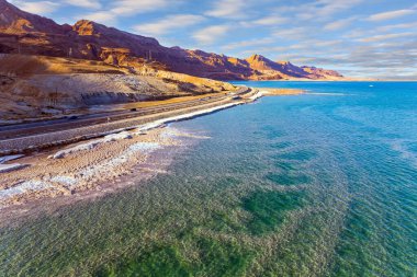 Asfalt karayolu sahil boyunca uzanıyor. Ölü Deniz, İsrail. Ölü Deniz, insansız hava aracından çekilmiş. Sahil boyunca buharlaşmış tuz birikmiş. Kışın akşam alacakaranlığı 