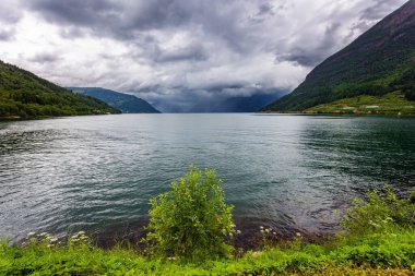 İskandinavya. Yaz, Temmuz. Güçlü bulutlar fiyordun su yüzeyine yansıyor. Hardangerfjord 'un başlangıcı. Batı Norveç 'in Dağları.