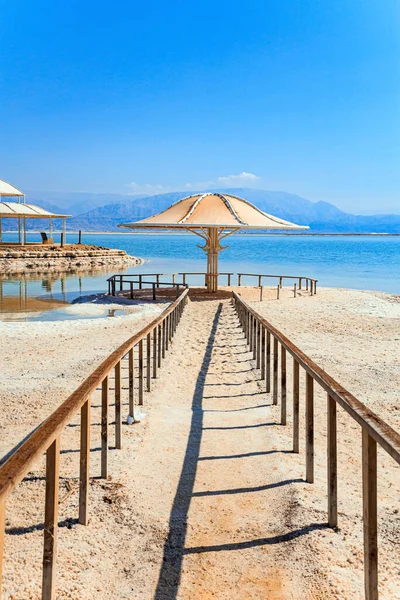 美しい丸い傘は太陽から保護します 中東の排水のない塩湖 死海だ イスラエルの海岸 レールは水へのパスを囲みます — ストック写真