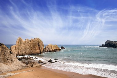 Kar beyazı deniz köpüğü donuk sonbahar güneşinde parlar. Cantabria, İspanya. Playa de la Arnia plajı. İnanılmaz jeolojik oluşumlar turistleri şaşırtır. Kıyı kayalarında fırtına dalgaları kopuyor.. 