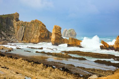 Cantabria, İspanya. Playa de la Arnia plajı. İnanılmaz jeolojik oluşumlar turistleri şaşırtır. Kıyı kayalarında fırtına dalgaları kopuyor. Kar beyazı deniz köpüğü parlıyor 