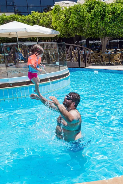 Family vacation in a hotel on the Greek island of Cyprus. Dad and little daughter joyfully swim together, dive and laugh. Great swimming pool. Happy family